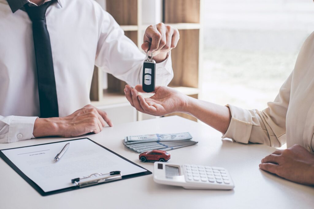 Business professional handing car keys to a client over a table with cash, a calculator, and a contract, illustrating car finance options.