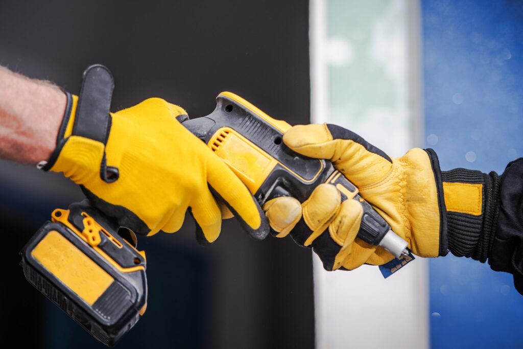 Hands in yellow gloves exchanging a power tool, symbolising collaboration in the tradie sector, relevant to home loan discussions for casual workers and tradies.