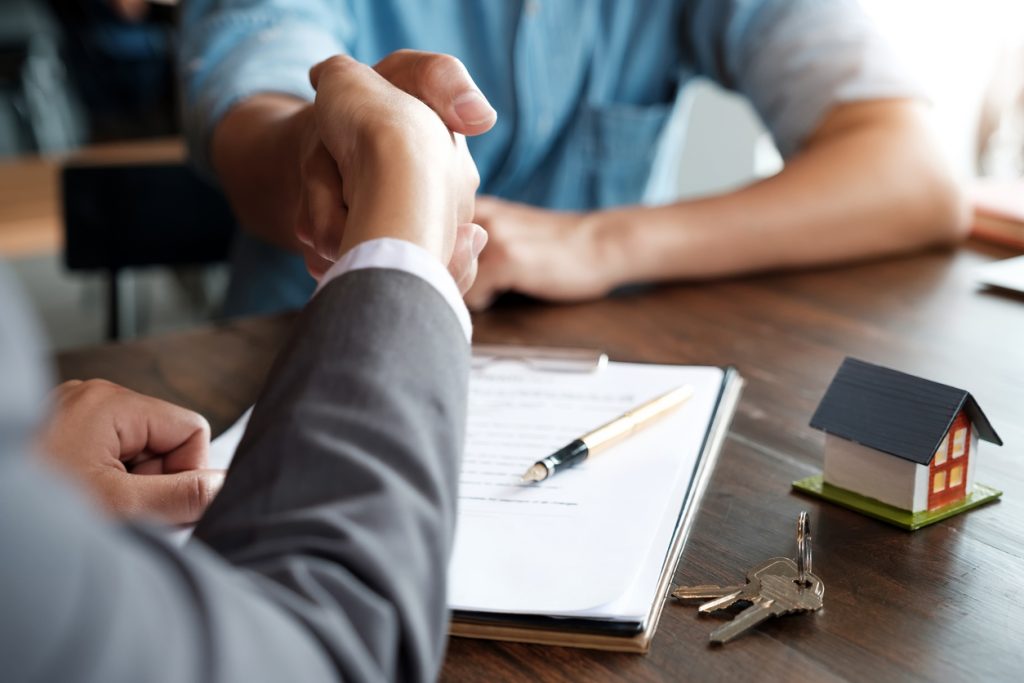 Handshake over mortgage documents with house model and keys, symbolising financial agreements and home financing options.