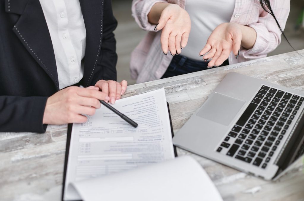 Two individuals discussing mortgage options, one pointing at a document and the other gesturing, with a laptop and paperwork on the table, illustrating the process of securing home financing.