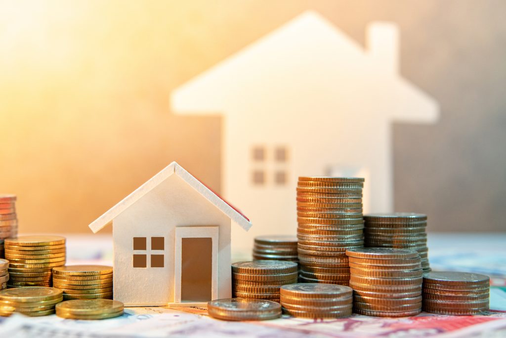 Model house surrounded by stacks of coins and banknotes, symbolising investment and financing options for home loans and property purchases.