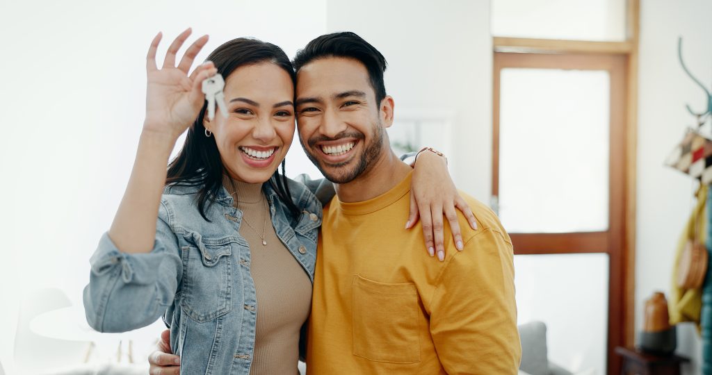 Happy couple celebrating home ownership, holding keys in a bright, modern interior, symbolizing first home loan success.