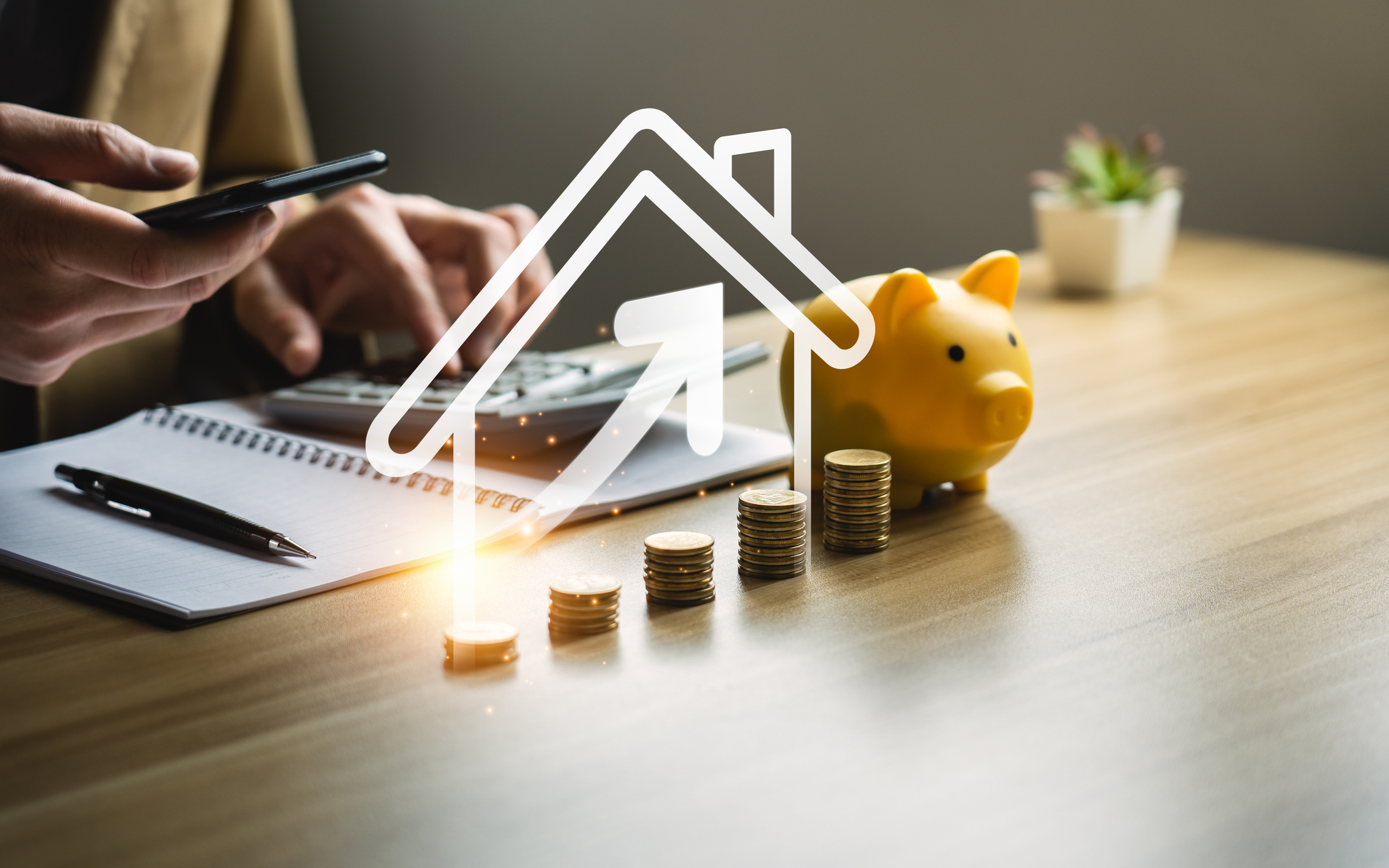 Person using a smartphone and calculator next to a piggy bank and stacked coins, symbolizing investment loans and financial growth in property purchasing.