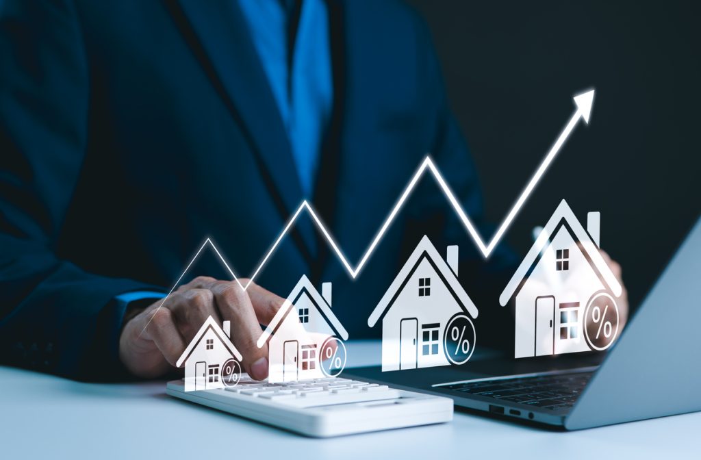 Businessman analysing mortgage options on a laptop, with graphical representation of rising house values and interest rates.