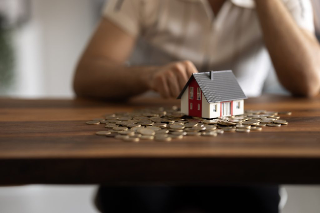 Model house on a table surrounded by coins, symbolising financial considerations in home loans and refinancing options.