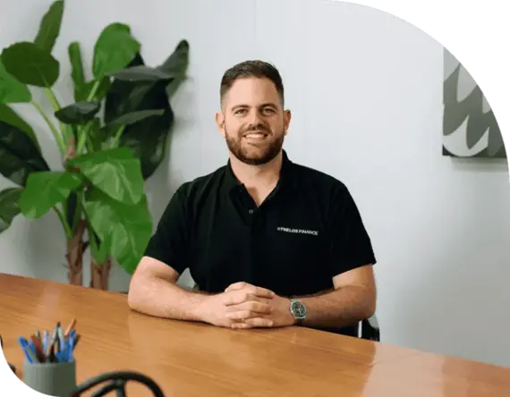 Man in a black Trelos Finance polo shirt seated at a wooden table, surrounded by greenery, representing personalised financial services and mortgage brokerage expertise.