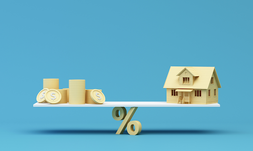 Wooden house model and stacks of coins balanced on a scale with a percentage symbol, representing refinancing home loans and financial considerations for Sydney borrowers.