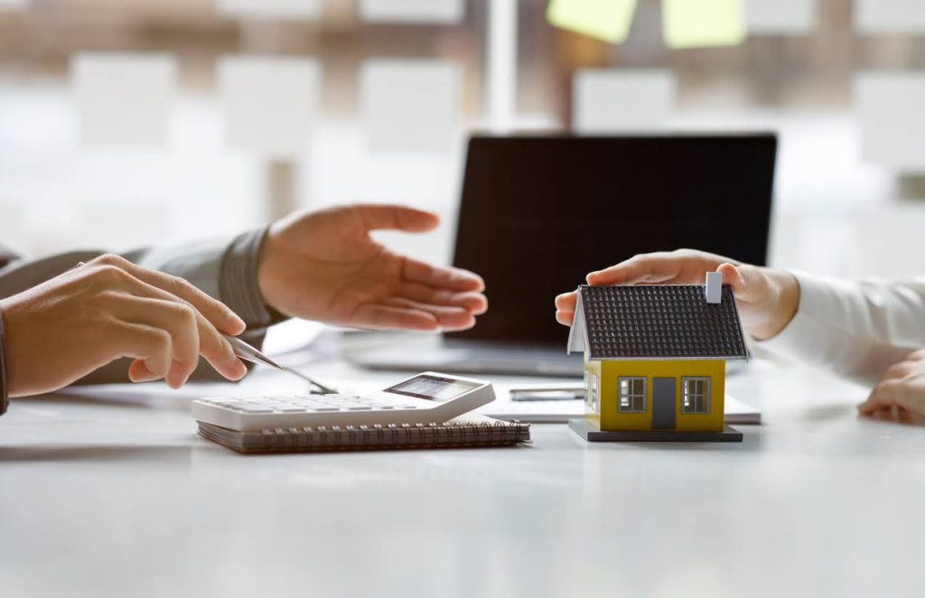 Hands discussing home loan options with a calculator and model house on a desk, representing refinancing and mortgage consultations in Sydney.