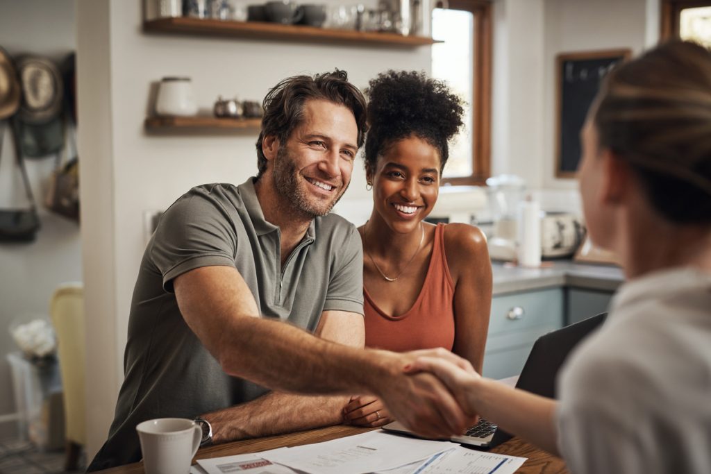 Couple shaking hands with a financial advisor in a home setting, discussing home loan options and mortgage advice in Australia.