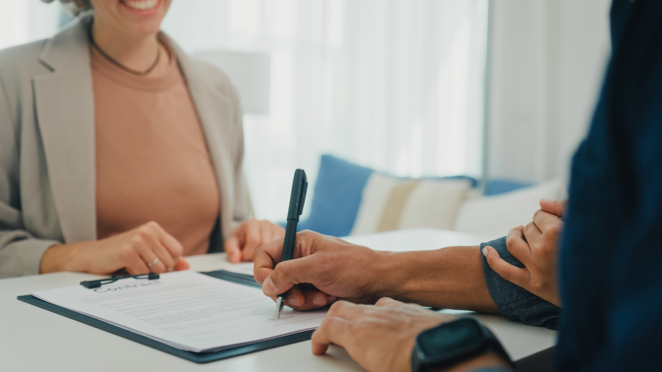 Woman in business attire smiling while a man signs a document, representing SMSF property investment consultation.